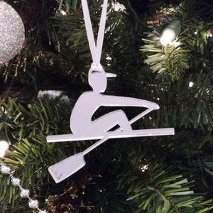 May include: White silhouette ornament of a person rowing a boat. The ornament is hanging on a Christmas tree.