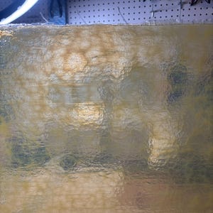 May include: A close-up view of a textured, translucent, golden-yellow surface. The surface has a rippled appearance, with subtle variations in color and tone. The texture appears to be slightly uneven, creating a play of light and shadow.