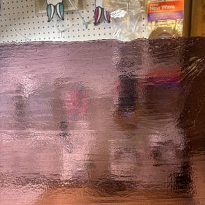 May include: A close-up of a sheet of pinkish-brown, textured material. The surface has a glossy sheen and appears to be reflective. The material has a slightly uneven texture with visible imperfections and lines. The color varies slightly across the surface.