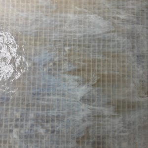 May include: A close-up view of a textured surface with a grid pattern. The surface has a light, neutral color palette with hints of blue and white, creating a subtle, flowing effect. The top edge features a beige, grid-like structure.