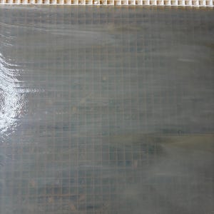May include: A close-up shot of a light gray, grid-patterned surface, possibly tile or a similar material. The surface is partially wet, with visible streaks and a reflective quality. At the top, a white, grid-like structure is present.