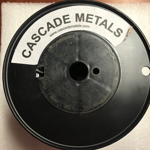 May include: A black spool of wire with a white label that says "CASCADE METALS" and "www.cascademetals.com".