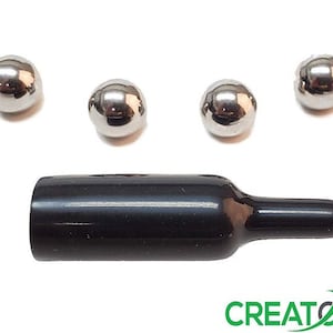May include: A black bottle stopper with a tapered end, accompanied by six shiny, silver-colored metal balls. The stopper is positioned horizontally, and the balls are arranged above it. The word "CREATOR'S" is visible at the bottom.