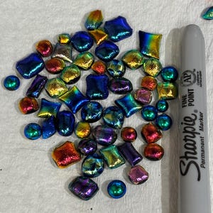 May include: A collection of iridescent glass pieces in various shapes and sizes, including squares, circles, and irregular forms. The colors shift from blue to gold, red, and purple. A gray Sharpie marker is included for scale.