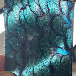 May include: A rectangular piece of resin art featuring a repeating pattern of overlapping, scale-like shapes in deep shades of teal, emerald green, and dark blue. The surface has a glossy, reflective finish with subtle metallic shimmer throughout.