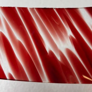 May include: A rectangular sheet of stained glass featuring a vibrant red and white marbled pattern. The glass displays diagonal streaks of opaque white swirling through a translucent deep red base, creating a fluid, wave-like visual effect.