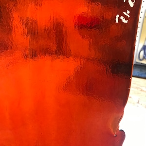 May include: A close-up of a bright orange, metallic, textured surface. The surface has a slight curve and a small tear in the lower right corner. The text "22.21" is written in white on the upper right corner.
