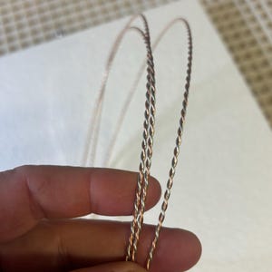 May include: Two strands of twisted wire, one silver and one copper, are shown in a close-up image. The wires are held in a hand, and the image is focused on the wire itself.