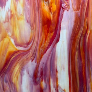 May include: Abstract glass art with a flowing design. The artwork features a blend of colors, including shades of red, orange, and white, creating a dynamic and fluid visual effect. The glass appears to have a glossy finish.
