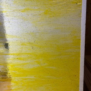 May include: A rectangular sheet of yellow stained glass with a textured surface. The glass has a semi-transparent appearance with small air bubbles throughout. The edges of the glass are straight and the color is a vibrant yellow.