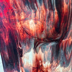 May include: A rectangular sheet of stained glass featuring a marbled pattern of deep crimson, dark burgundy, and black swirls blended with translucent white areas. A small rectangular sticker with the text (412) 628-3000 is visible at the top.