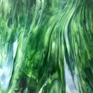 May include: A sheet of stained glass with a flowing, marbled pattern in shades of green and white. The glass has a translucent quality, with light passing through the swirling colors. The design resembles a natural landscape.