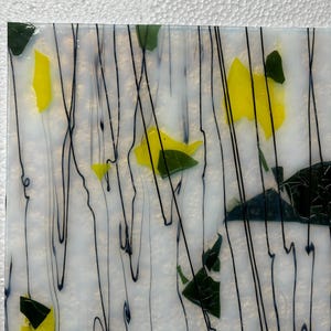 May include: Abstract glass art piece with a white background, featuring yellow and green shapes, and black, wavy lines. The design is reminiscent of a floral or natural theme, with a textured appearance.