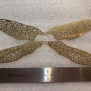 May include: Four gold metal dragonfly wings with a delicate, intricate design. The wings are about 7 inches long and are arranged in a symmetrical pattern.