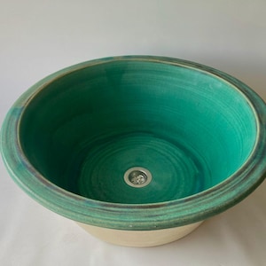 Può includere: Un lavandino in ceramica con una smaltatura verde e un bordo bianco. Il lavandino ha un foro di scarico al centro.