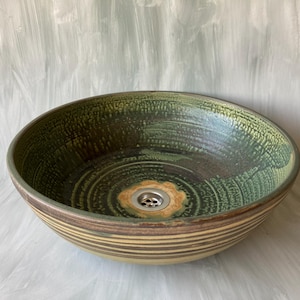 Può includere: Un lavandino in ceramica verde e marrone con uno scarico bianco. Il lavandino ha un motivo a strisce intorno al bordo.