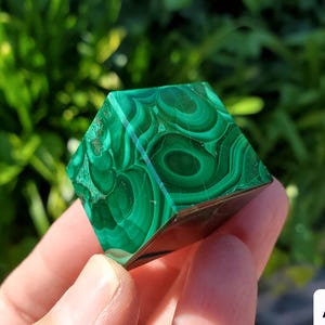 Può includere: Un cubo di malachite verde con motivi a spirale. Il cubo è lucido e ha una superficie liscia.