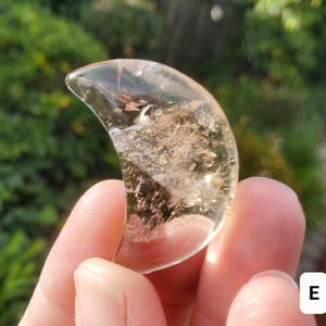 Pode incluir: Um cristal transparente em forma de crescente com uma tonalidade dourada. O cristal tem uma superfície lisa e polida e é segurado na mão.