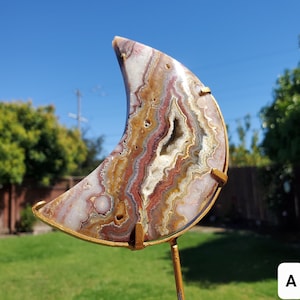 Könnte beinhalten: Ein sichelförmiger Achat-Geode mit einem goldenen Metallständer. Der Achat ist eine Mischung aus Weiß, Braun, Rot und Rosa mit einer natürlichen Kristallhöhle in der Mitte.