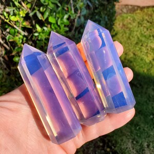 Könnte beinhalten: Drei regenbogenfarbene violette Kristallspitzen mit einem hellblauen und goldenen Schimmer. Die Spitzen sind in einer Reihe angeordnet, wobei die größte Spitze in der Mitte liegt.