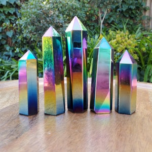 May include: Five iridescent rainbow titanium quartz crystal points arranged in a row on a wooden surface. The crystals are all different sizes and shapes, but they all have a similar iridescent rainbow effect.