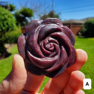 May include: A carved rose-shaped gemstone pendant in shades of purple and pink. The gemstone is polished and has a smooth, glossy finish.