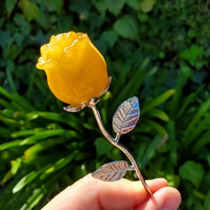 Peut inclure: Une rose jaune en ambre avec une tige et des feuilles en argent.