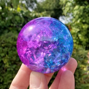 May include: A clear glass sphere with a swirling pattern of purple and blue crystals. The sphere is about the size of a golf ball.