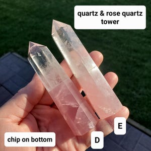 May include: Two quartz and rose quartz towers are held in a hand. The towers are a pale pink color and have pointed tops. The text "quartz & rose quartz tower" is in a white box at the top. The text "chip on bottom" is in a white box at the bottom.