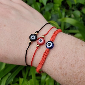 May include: Three red string bracelets with evil eye charms. The charms are black, red and blue.