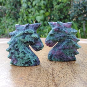 May include: Two green and purple horse head sculptures carved from zoisite gemstone. The sculptures are facing each other.