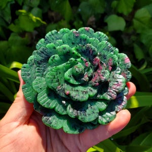 Könnte beinhalten: Eine grüne und rosafarbene geschnitzte Blume aus Edelstein. Die Blume hat mehrere Blütenblätter und ist aufwendig verziert.