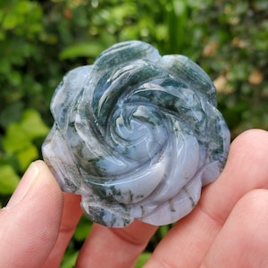 Puede incluir: Una rosa tallada en ágata verde y blanca. La rosa está tallada en un patrón de espiral y tiene un patrón de ágata natural.