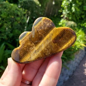 May include: A golden brown tiger's eye crystal carved into a cloud shape. The crystal has a striated pattern and a glossy finish.