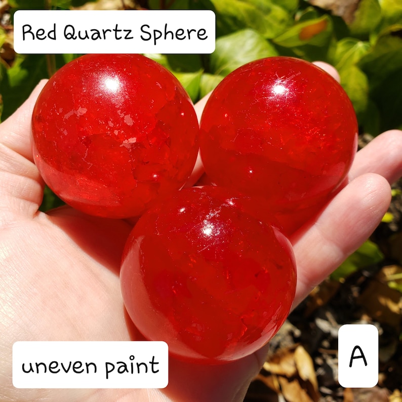 May include: Three red quartz spheres with uneven paint are displayed. The spheres are a vibrant red color and appear to be translucent. The text "Red Quartz Sphere" and "uneven paint" are visible in the image.