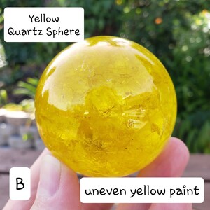 May include: A yellow quartz sphere with uneven yellow paint. The sphere is round and appears to be made of a translucent material. Text on the image reads "Yellow Quartz Sphere" and "uneven yellow paint".