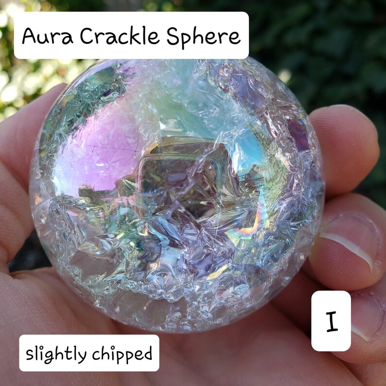 May include: Aura Crackle Sphere with iridescent colors. The clear sphere has a cracked texture and is slightly chipped. The text "Aura Crackle Sphere" is at the top, and "slightly chipped" is at the bottom.