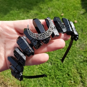 Può includere: Fascia per capelli in cristallo di ossidiana nera con un ciondolo a forma di mezzaluna d'argento. La fascia è realizzata in elastico nero ed è adornata da un gruppo di cristalli di ossidiana nera.