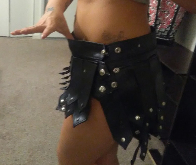 May include: Black leather skirt with silver-tone rivets and decorative cutouts. The skirt has a high waist and a layered design, fastened with multiple snaps. The skirt's edgy design is suitable for cosplay or alternative fashion.