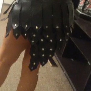 May include: Black leather skirt with a layered, segmented design. The skirt features small, silver-colored studs and a unique, edgy aesthetic. The skirt is a mini-skirt style.