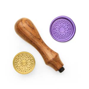 May include: A wooden handle wax seal stamp with two wax seals. One seal is gold with a detailed design and the other is purple with a similar design.