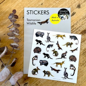 May include: A sticker sheet with illustrations of Tasmanian wildlife, including a kangaroo, Tasmanian devil, and echidna. The sheet is labelled "STICKERS Tasmanian Wildlife". A yellow circle reads "Made in Australia". The stickers are on a wooden surface.