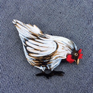 May include: A white and brown painted wooden chicken figurine with a red comb and wattle. The chicken is looking down and has its wings spread out.