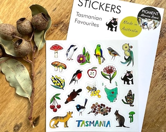May include: A sheet of stickers featuring Tasmanian wildlife and flora. The stickers are colorful and feature illustrations of animals like a Tasmanian devil, a platypus, a bird, and a quoll. There are also stickers of plants like wattle, gum nuts, and a red flowering plant. The stickers are labeled "Tasmanian Favourites" and "Made in Australia".