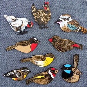May include: A set of nine wooden bird and chicken ornaments. The ornaments are painted in various colors, including black, white, red, yellow, blue, and brown. The ornaments are all different shapes and sizes, and they are all very detailed.