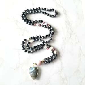 May include: A black and white gemstone mala necklace with a labradorite pendant. The necklace features pink and white accent beads.