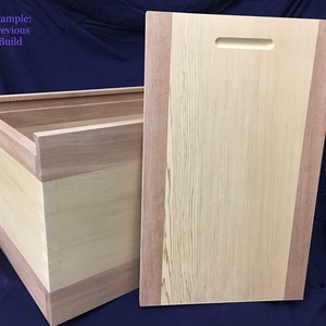 May include: A wooden box with a lid, constructed from light-colored wood with darker wood accents. The lid has a handle cut into it. The box is rectangular and appears to be handmade.