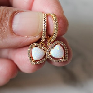Puede incluir: Pendientes de oro en forma de corazón con piedras de ópalo blanco y un halo de cristal transparente.