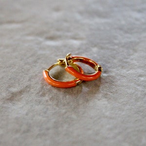 Op de afbeelding: Een paar gouden oorringen met een feloranje emaille coating.