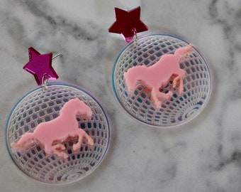 May include: A pair of pink and clear acrylic earrings featuring a pink horse silhouette on a disco ball design with a pink star charm.